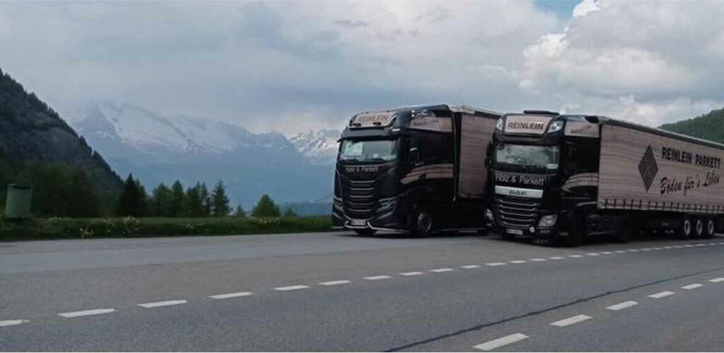 Reinlein Parkett - Zwei Transporter auf der Straße vor Bergen